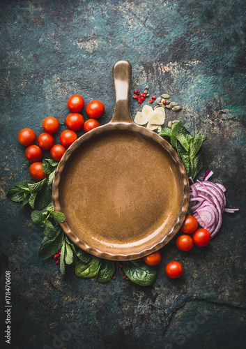 Vegetarian cooking ingredients around frying pan on dark rustic background, place for text, frame. Healthy eating and cooking, clean or diet food concept