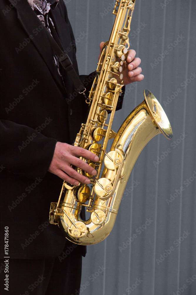 Naklejka premium Hands of groom play on saxophone on grey background