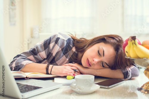 Exhausted woman fell asleep while working on laptop at home.