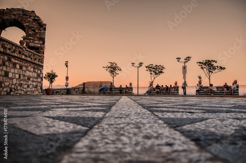 PIazza con pavimento chiaro scuro al tramonto con visitatori che si riposano su panchine photo