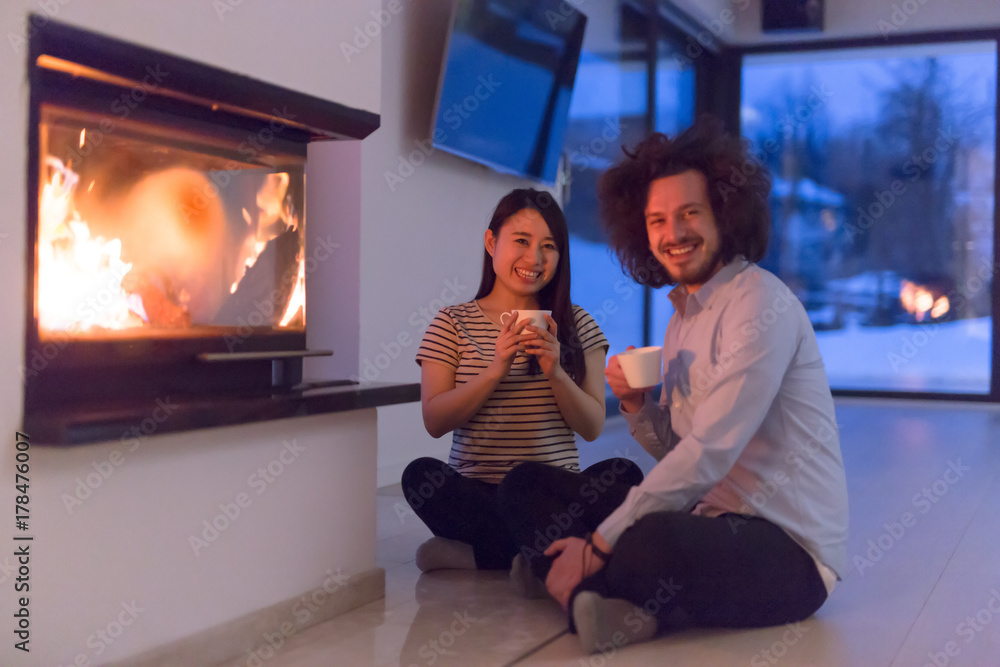 happy multiethnic couple sitting in front of fireplace