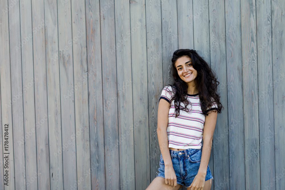 Fototapeta premium Beautiful smiling woman wearing casual clothes, posing outdoors near a wall