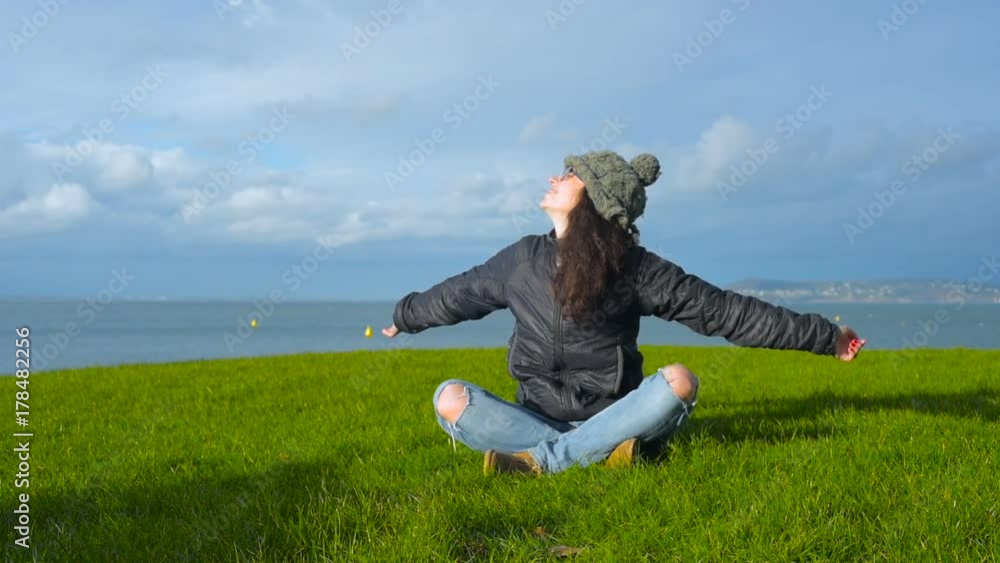 young happy smiling woman enjoying the spring sun sitting on green grass on seaside. Slow motion young happy smiling woman enjoying the spring sun sitting on green grass on seaside. Slow motion