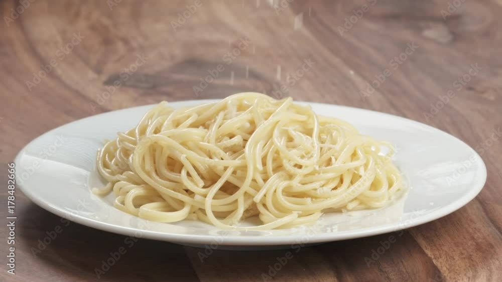 Slow motion grated aged parmesan cheese falling on spaghetti