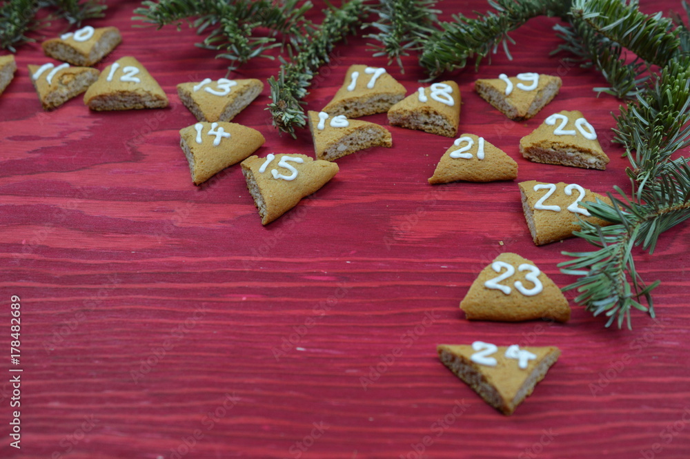 twenty-four numbered advent cookies on red wood with pine boughs
