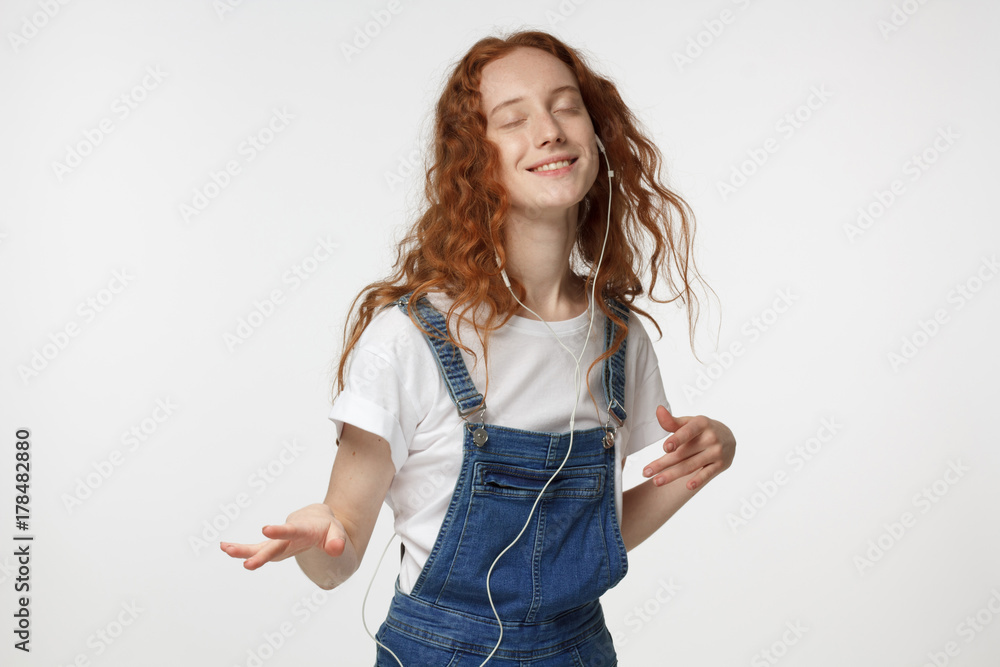 Catch the rythm. Feel th vibe. Redhead girl with beautiful smile, in blue jumpsuit, dancing, listening to his favourite song Catch the rythm. Feel th vibe. Redhead girl with beautiful smile, in blue jumpsuit, dancing, listening to his favourite song