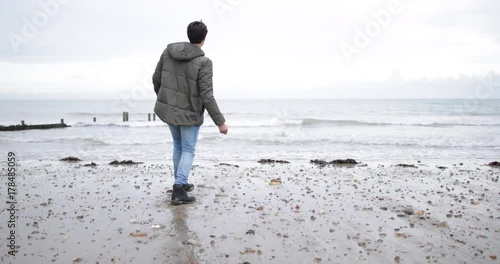 Young male skimming stones on a beach in winter