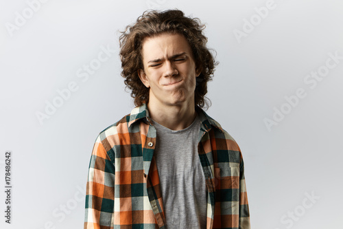Foto Portrait of handsome young man dressed stylishly having painful look, pursing lips and frowning, can't hide his pain or bad mood