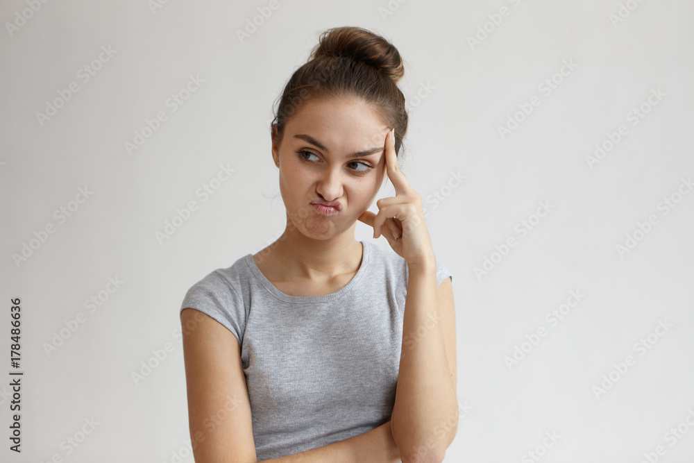 Thoughtful pensive young woman with hair bun making displeased grimace as if saying No, that's not an option while trying to solve problem, thinking over decision, holding head and looking sideways Thoughtful pensive young woman with hair bun making displeased grimace as if saying No, that's not an option while trying to solve problem, thinking over decision, holding head and looking sideways