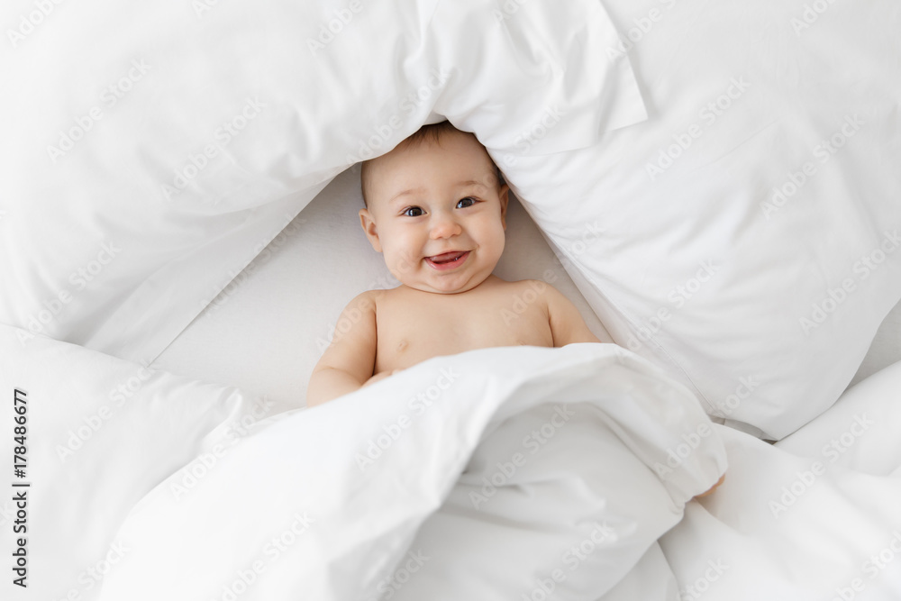 Smiling baby lying on back in white sheets Smiling baby lying on back in white sheets