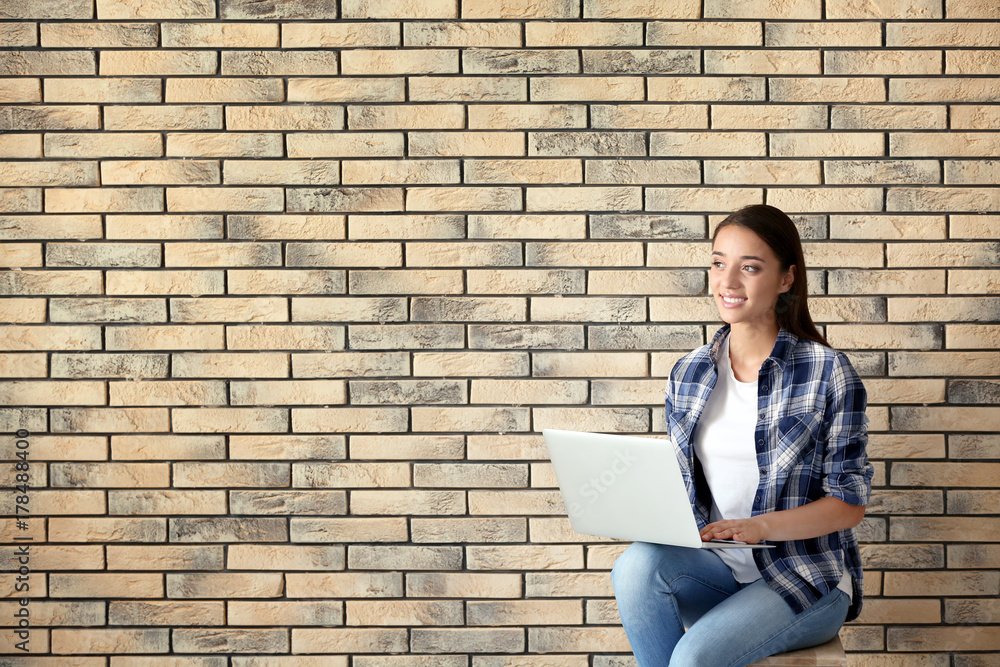 Pretty woman with modern laptop sitting on chair near brick wall Pretty woman with modern laptop sitting on chair near brick wall
