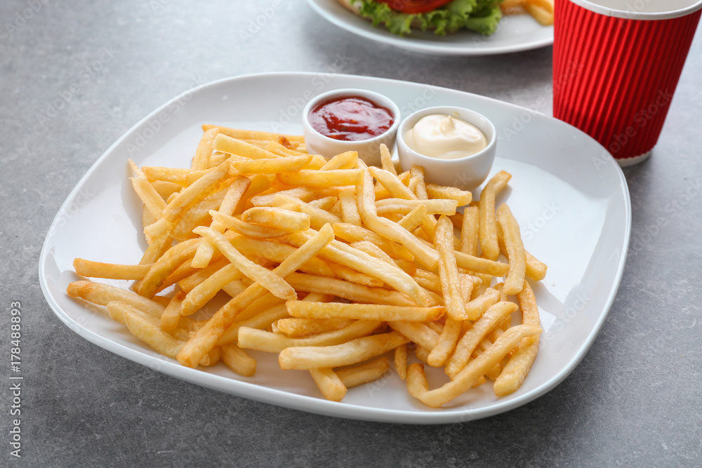 Plate with yummy french fries and sauces in small bowls on table