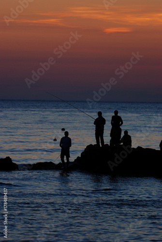 на закате рыбаки ловят удочкой в море с берега
