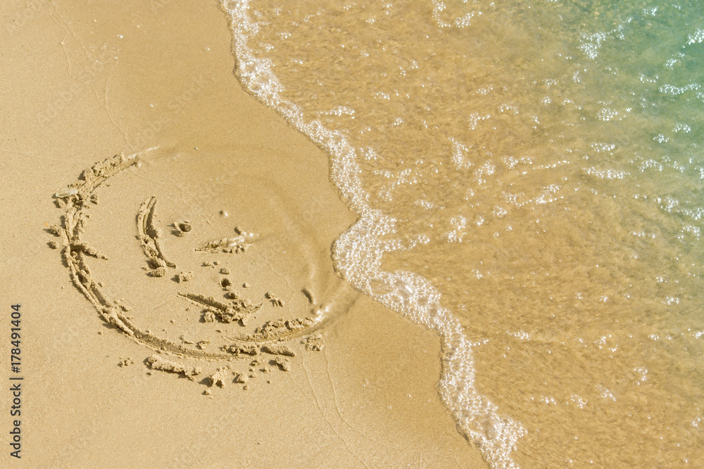 Obraz premium Children's drawing on a sandy sea beach. Smiling face drawn on yellow sand