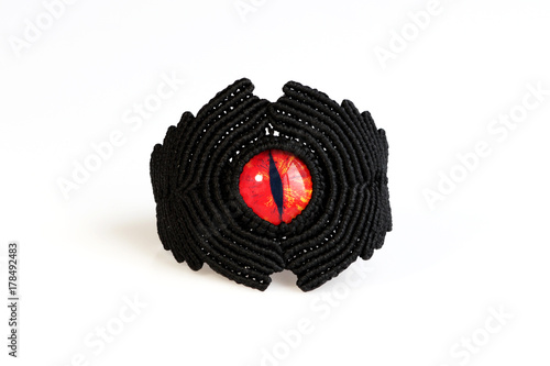 black bracelet for the hand from waxed thread, and red dragon eye in the technique of macrame on a white background.