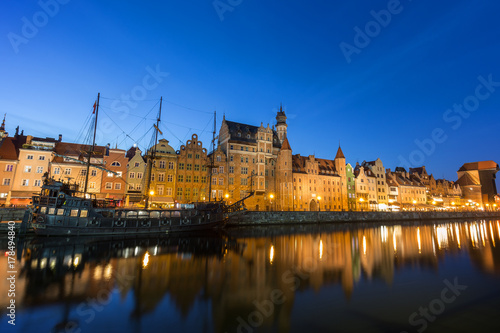 Scenic view of a tourist sailing boat and lit old buildings along the Long Bridge waterfront at the Main Town in Gdansk, Poland, in the evening.