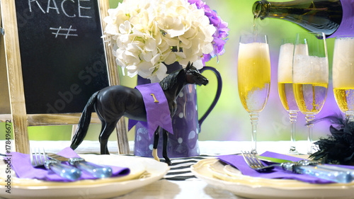 Horse racing Racing Day Luncheon fine dining table setting with small black fascinator hat, decorations and champagne, pouring champagne.