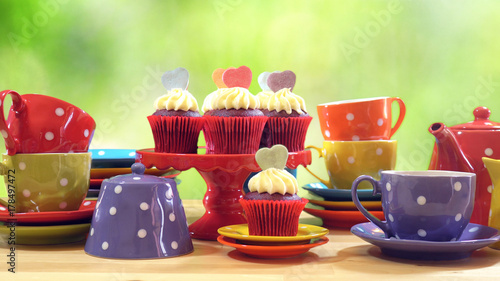 Colorful Mad Hatter style tea party with cupcakes and rainbow colored polka dot cups and saucers, with bokeh garden background and lens flare, with copy space.