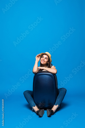 Young beauty woman sitting with travel baggage on the floor on blue background