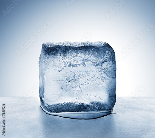 Frosty translucent, frigid cold blue ice block melting to create pool of water on scratched steel surface