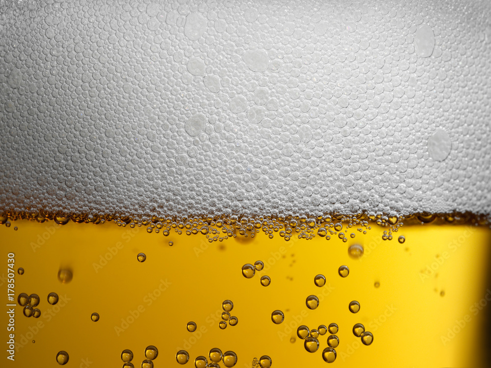 Closeup of freshly poured gold amber beer with frothy head and carbonation bubbles Closeup of freshly poured gold amber beer with frothy head and carbonation bubbles