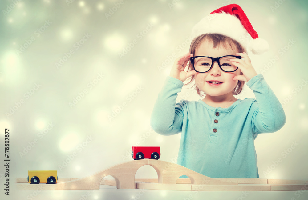 Φωτογραφία Happy toddler girl with a Santa hat and glasses playing with her toys