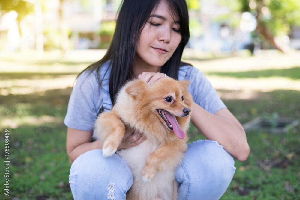 Cheerful asian young woman playing and happy fun with her dog at public park