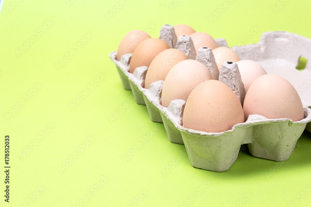 Chicken eggs in a cardboard box on a green background. Copy space for text
