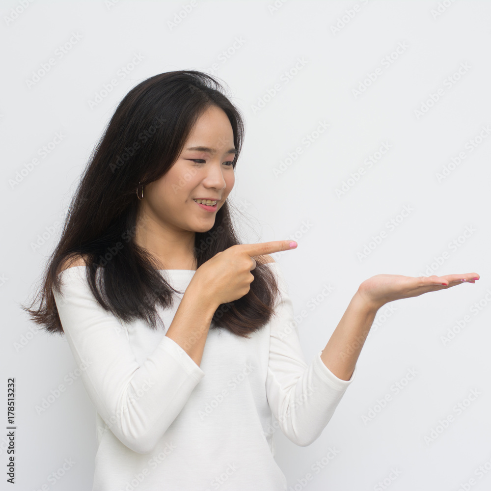 Asian girl shows a hand advertising. Woman with outstretched hand. Beautiful girl. Beautiful portrait of a girl in white shirt over a white background. Asian girl shows a hand advertising. Woman with outstretched hand. Beautiful girl. Beautiful portrait of a girl in white shirt over a white background.