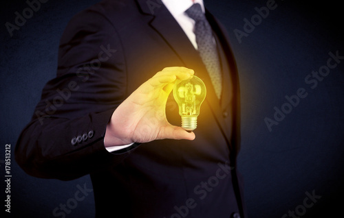 man in suit holding a glowing yellow light bulb