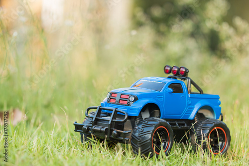 A scene of Blue RC Off-road truck car (Radio-controlled) is parked on the green grass with blurred meadow background. (This toy has some dust from children playing)