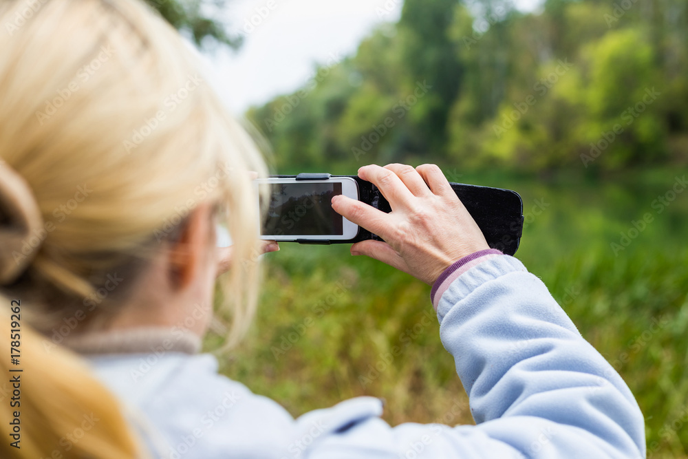 A blonde woman using a phone takes a photo of a beautiful landscape A blonde woman using a phone takes a photo of a beautiful landscape