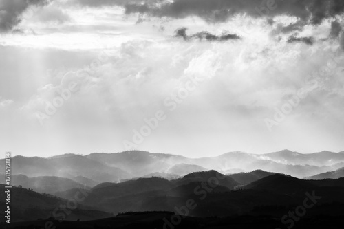 Various layers of hills and mountains with mist between them, with sun rays coming out through the clouds