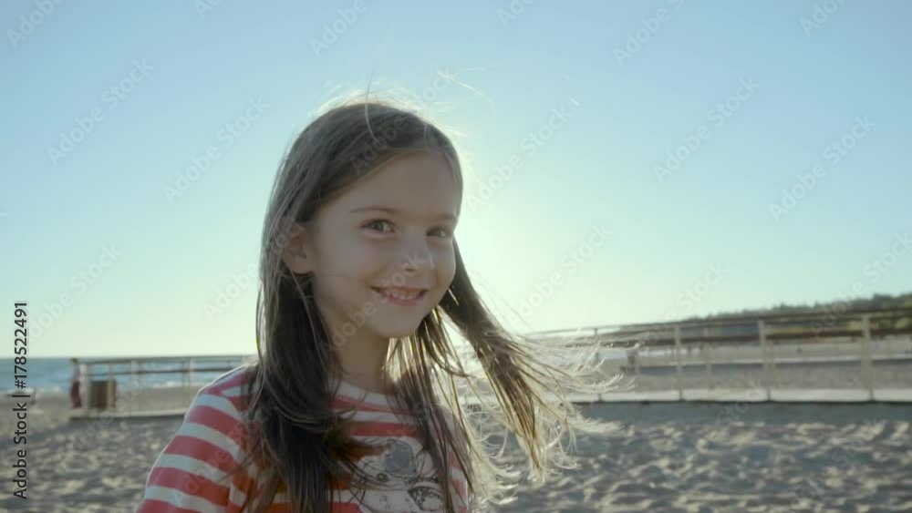 Happy small girl stands, runs, and falls on a sea beach, at sunset in slo-mo Happy small girl stands, runs, and falls on a sea beach, at sunset in slo-mo