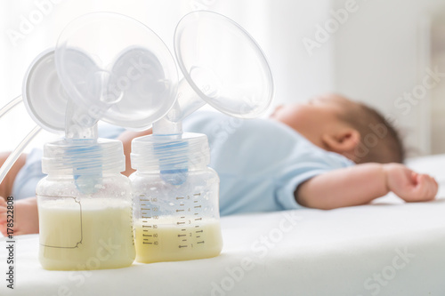 Breast milk pump and baby lying on the white bed photo