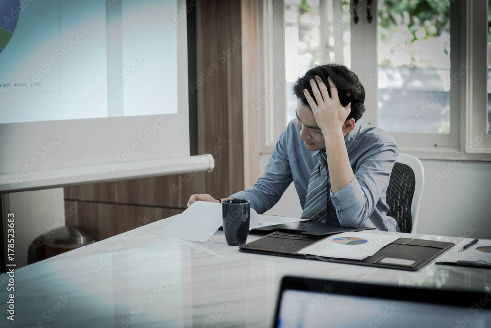 businessman having a hard time with coin stack, calculator and document graphic on the table, he holding his head in his hands. businessman having a hard time with coin stack, calculator and document graphic on the table, he holding his head in his hands.