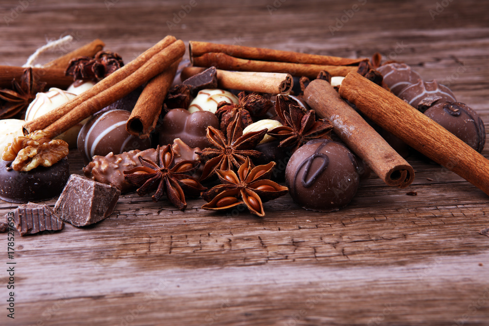 A selection of assorted chocolate truffle pralines on a wooden table with dark chocolate, cinnamon and anise.