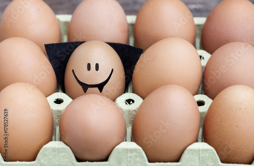 Smiling egg  dressed up as a vampire wearing souronded by blank brown eggs.