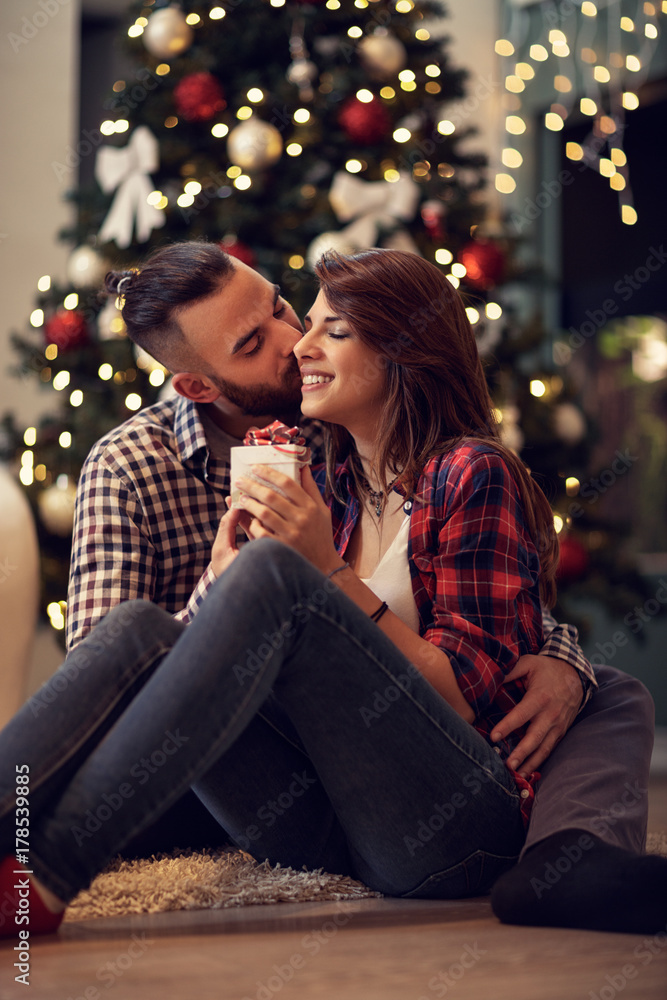 Husband hug and kisses his wife while gives her Christmas present Husband hug and kisses his wife while gives her Christmas present