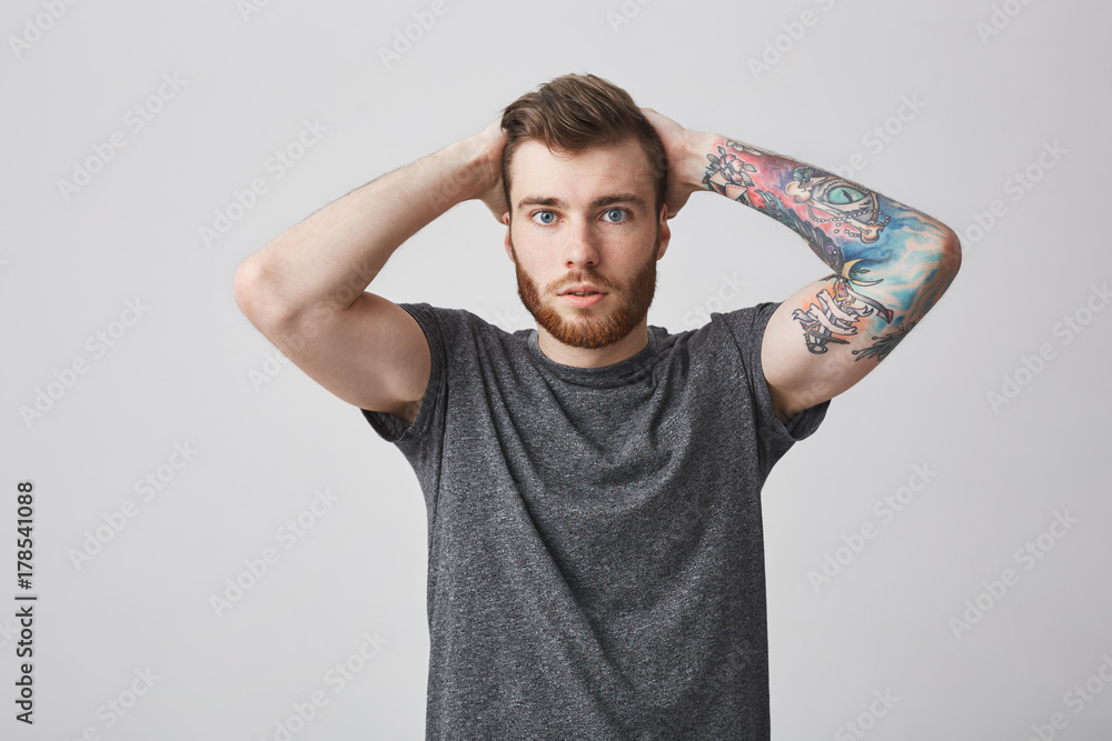 Beautiful fashionable bearded men with colored tattoo on arm and good  hairstyle holding hands behind head, looking in camera with confused and  surprised expression. Stock Photo | Adobe Stock