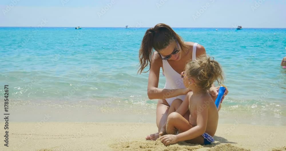 The best moments, the mother with a little daughter are played on the sea, in sunglasses, in swimsuit, sun protection cream, sea and sand background. Concept: love, lifestyle, children, vacations The best moments, the mother with a little daughter are played on the sea, in sunglasses, in swimsuit, sun protection cream, sea and sand background. Concept: love, lifestyle, children, vacations