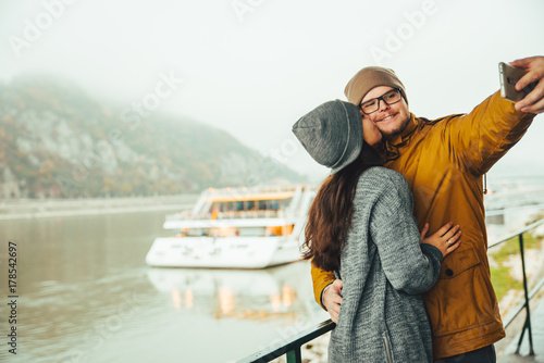 couple standing near river boat with mountain on bckground
