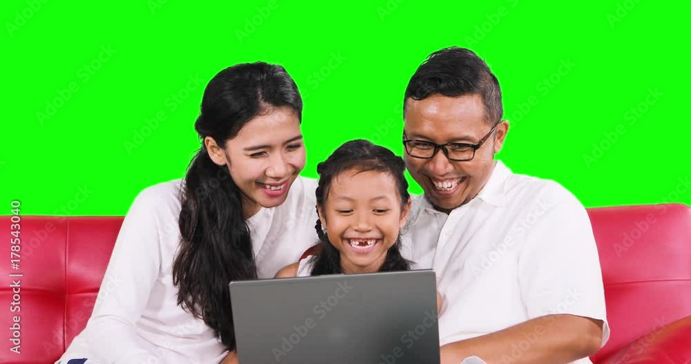 Toothless little girl and her parents using a laptop computer together while laughing and sitting on the sofa with green screen background. Shot in 4k resolution Toothless little girl and her parents using a laptop computer together while laughing and sitting on the sofa with green screen background. Shot in 4k resolution