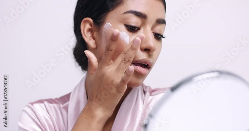 Pretty young Moroccan woman putting face cream on her cheeks and massages it into the skin isolated on white
