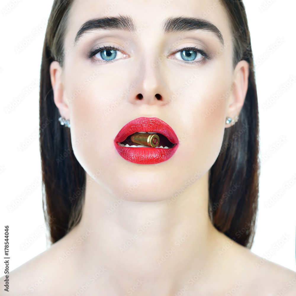 Beautiful young woman with shell in her lips. Blue-eyed girl with red lipstick holding bullet in her teeth. Beauty will save the World, danger, war concept. Beautiful young woman with shell in her lips. Blue-eyed girl with red lipstick holding bullet in her teeth. Beauty will save the World, danger, war concept.