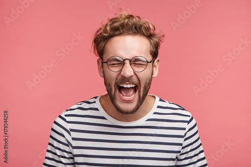 Isolated shot of overjoyed unshaven male screams in happiness, closes eyes and opens mouth, being glad to win tourist voucher, happy spend holidays abroad in exotic country, together with lover