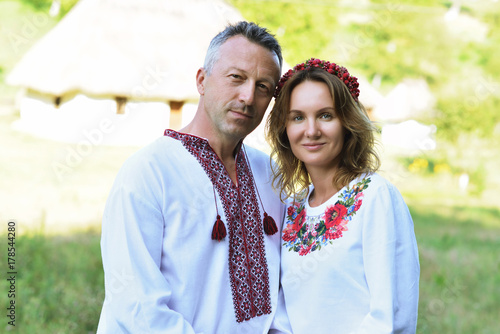 Ukrainian couple in traditional clothing vyshyvanka over landscape of tipical ucrainian village, summer outdoor. photo