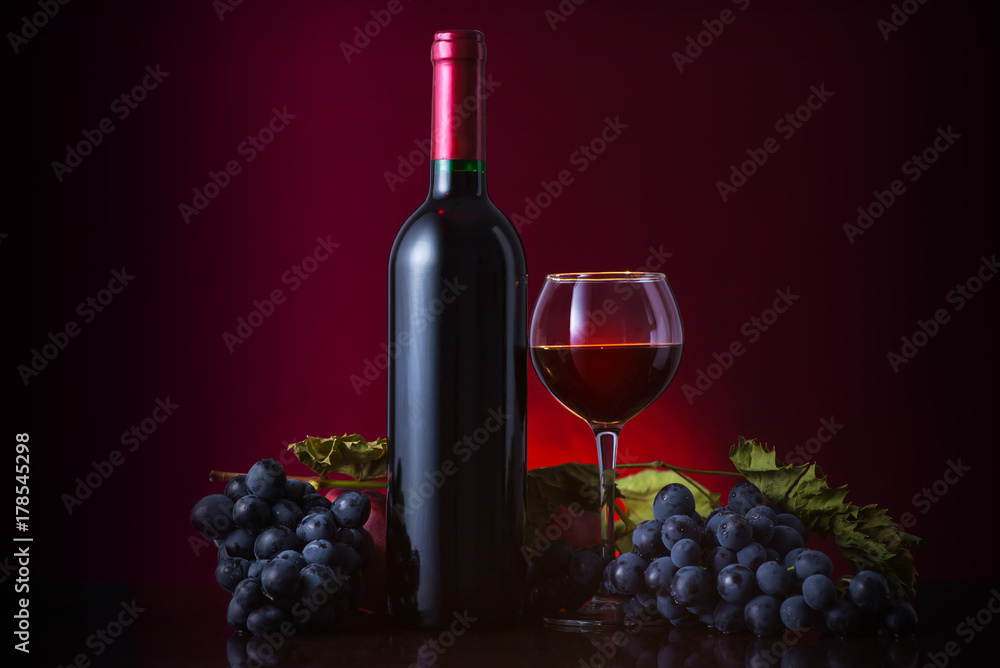 Wine. Bottle and glass of red wine with ripe grapes still life. Red wine on a dark background.