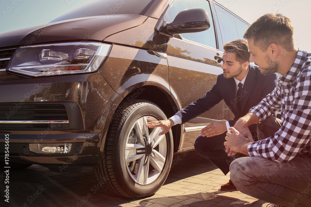 Salesman showing new car to customer outdoors Salesman showing new car to customer outdoors