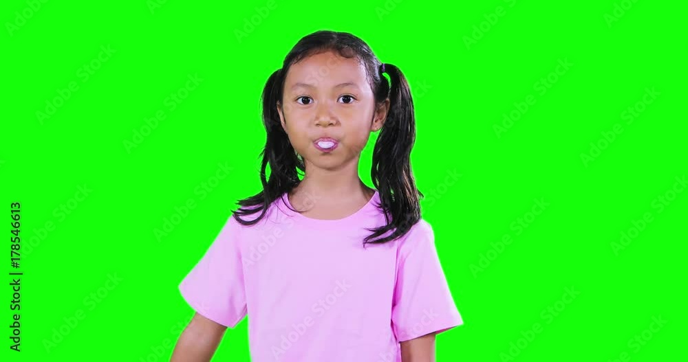 Funny little girl with pigtail hair, chewing gum in the studio with green screen background. Shot in 4k resolution
